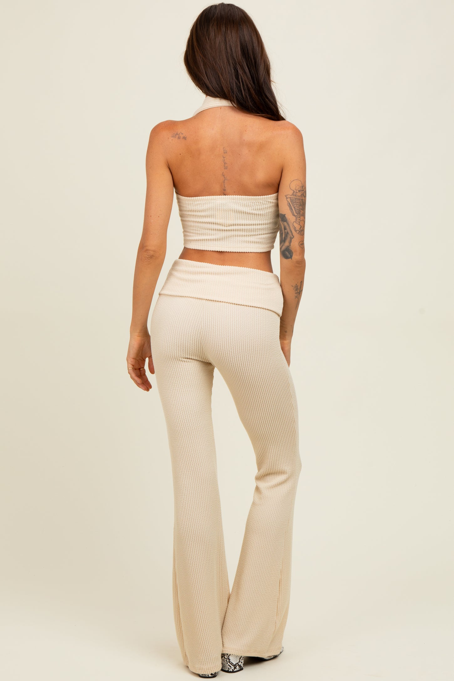woman wearing a beige ribbed two-piece set with a cropped halter top and flared pants, seen from the back