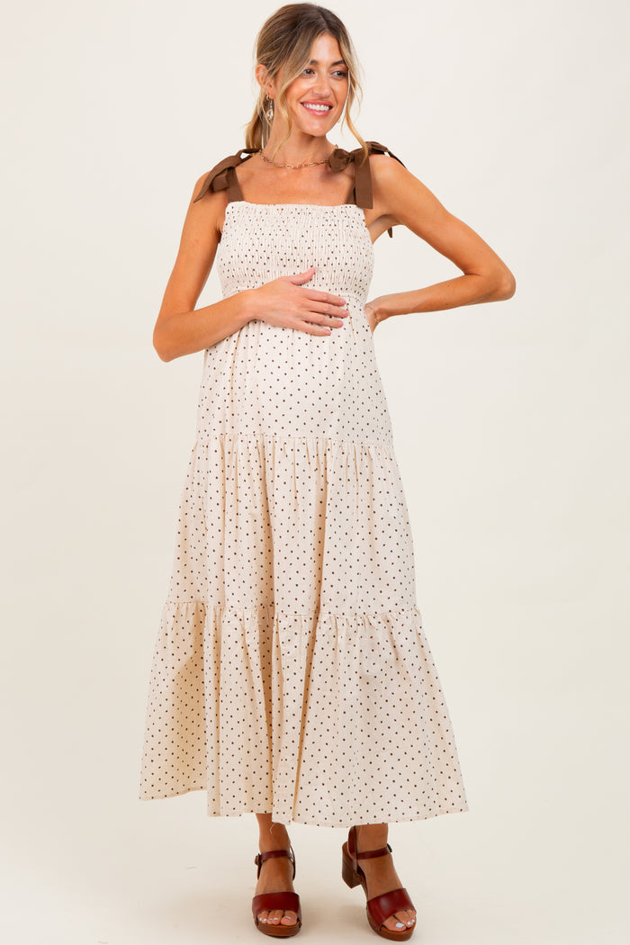 woman wearing a beige polka dot maternity maxi dress with tie straps and holding her baby bump
