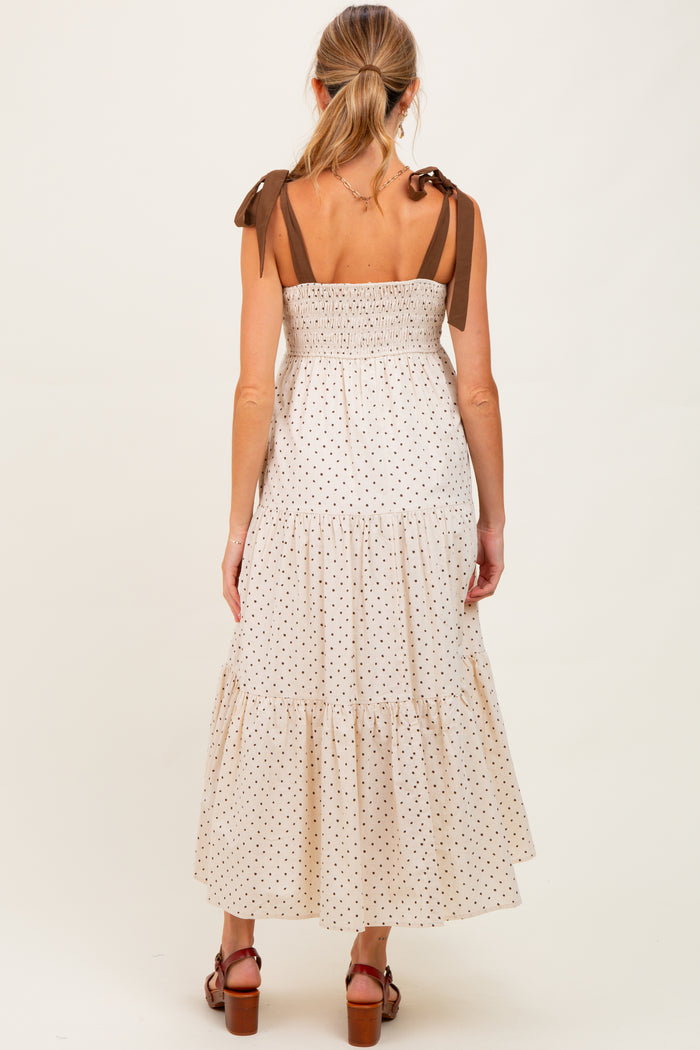 woman wearing a cream polka dot maternity maxi dress with brown tie straps and a smocked bodice, showing a baby bump from behind