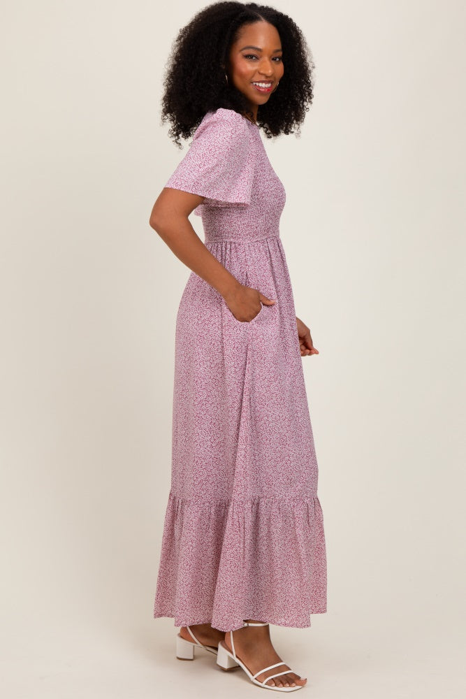 woman wearing a pink floral maxi dress with short sleeves and pockets, standing in profile against a neutral background