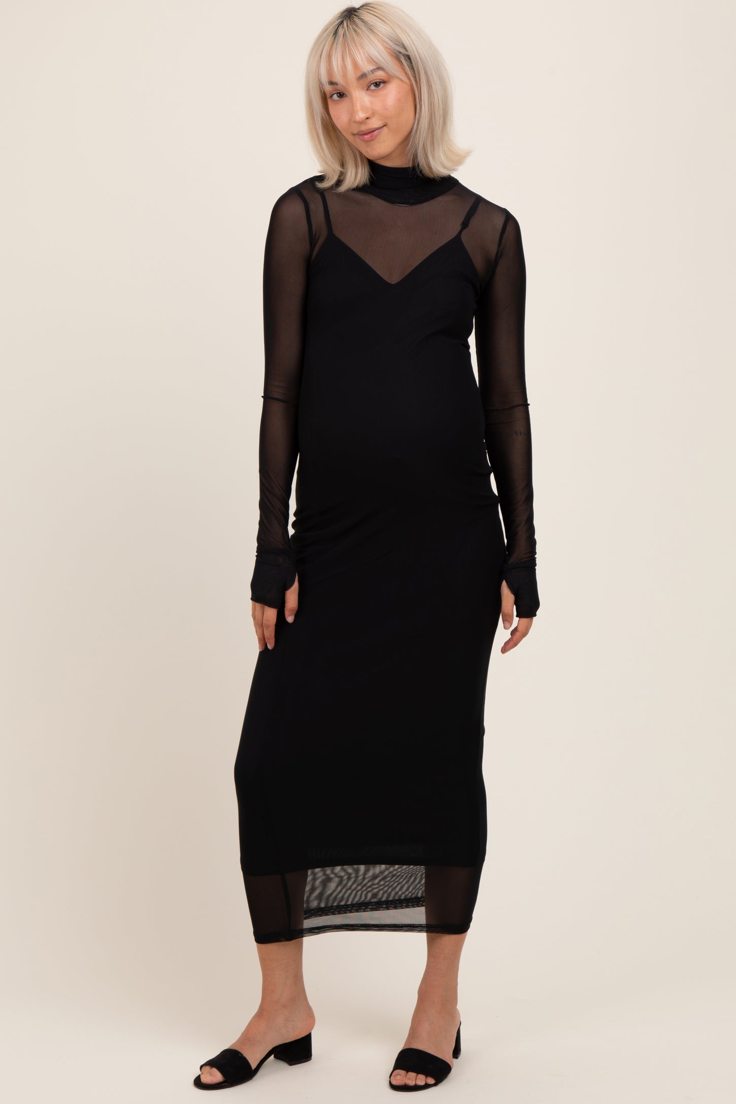 woman wearing a black maternity dress with sheer long sleeves and a fitted silhouette, showing her baby bump
