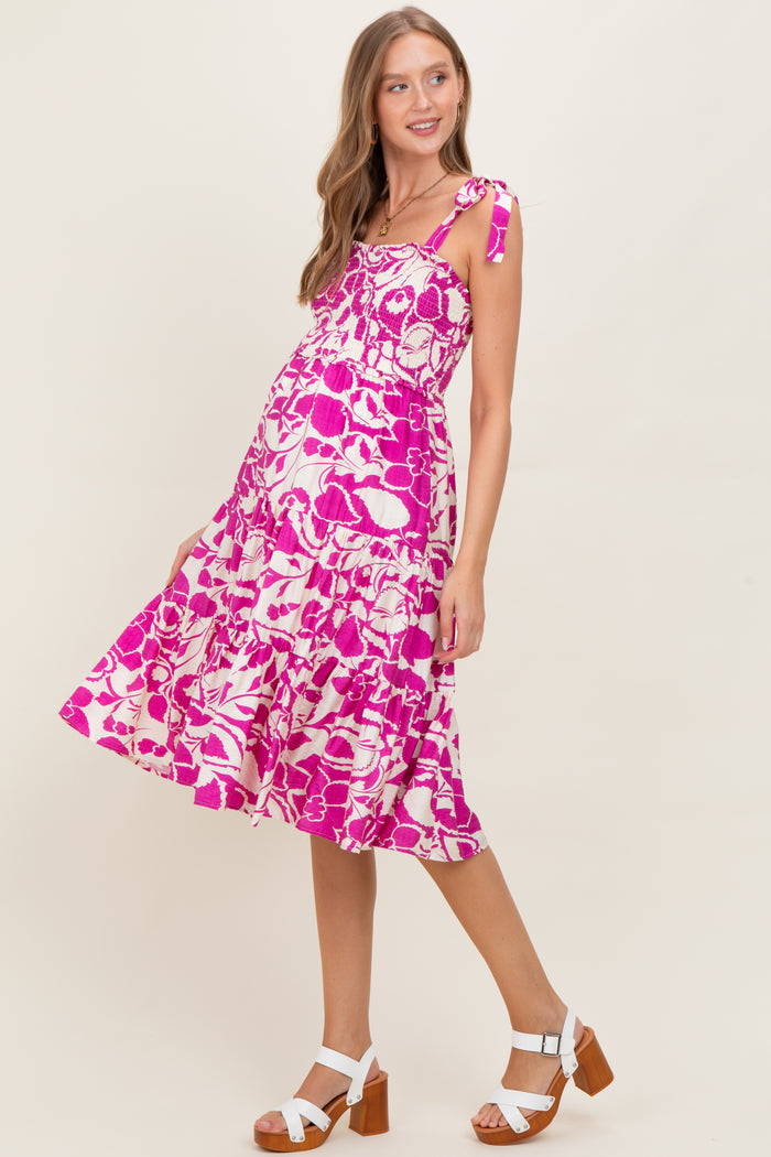 woman wearing a pink and white floral maternity dress with tie straps and a flowing skirt, showing her baby bump