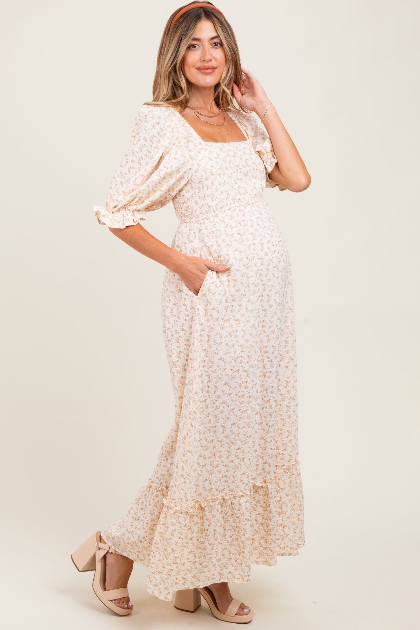 woman wearing a cream floral maternity maxi dress with puff sleeves and pockets, showing her baby bump