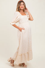 woman wearing a cream floral maternity maxi dress with puff sleeves and pockets, showing her baby bump