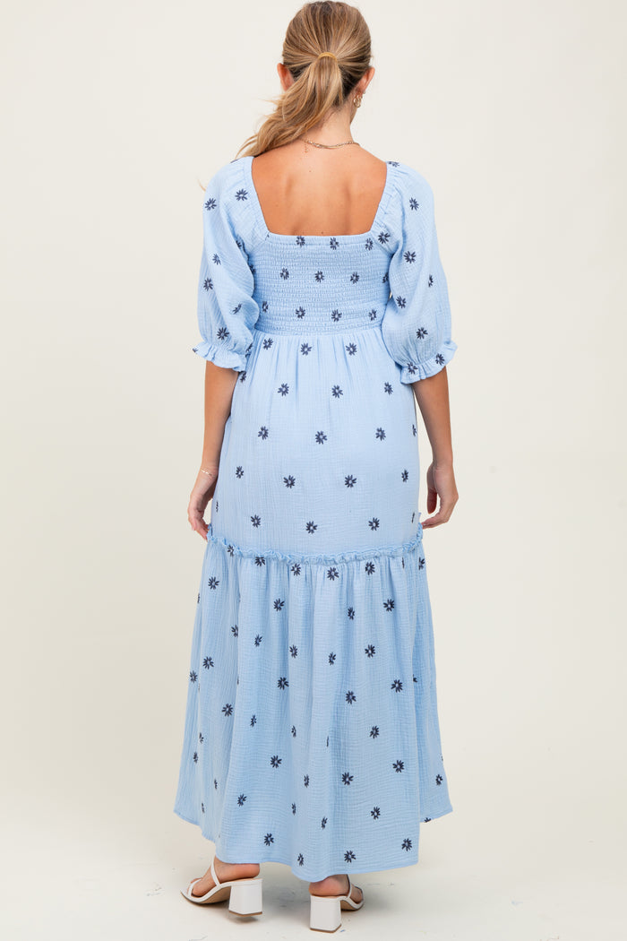 woman wearing a light blue maternity maxi dress with puff sleeves and floral embroidery on the back