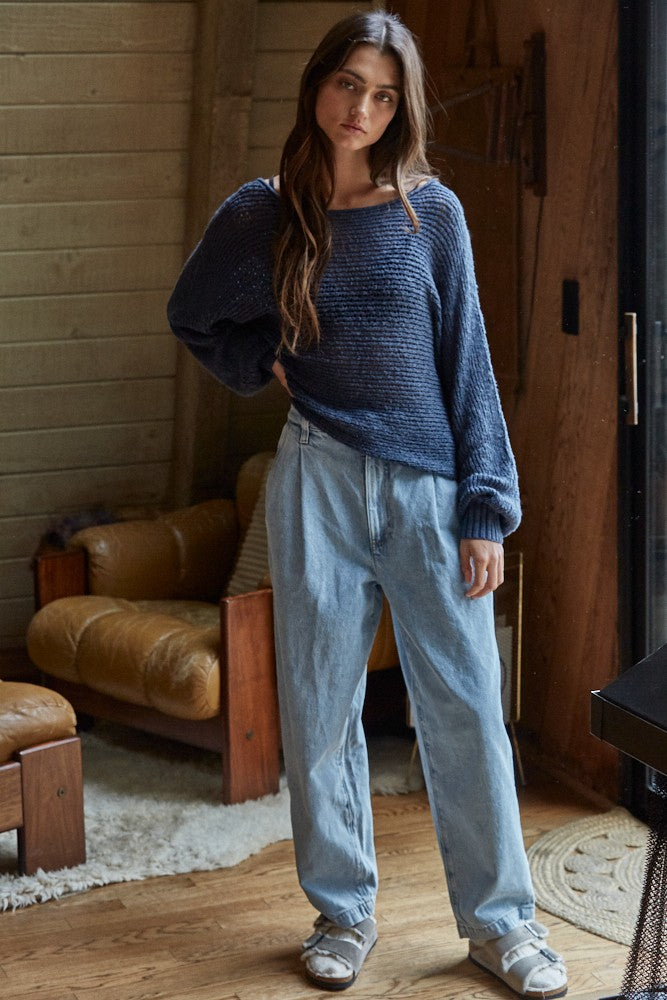 woman wearing a navy blue oversized knitted sweater and light blue baggy jeans, standing indoors with a casual look