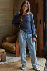 woman wearing a navy blue oversized knitted sweater and light blue baggy jeans, standing indoors with a casual look
