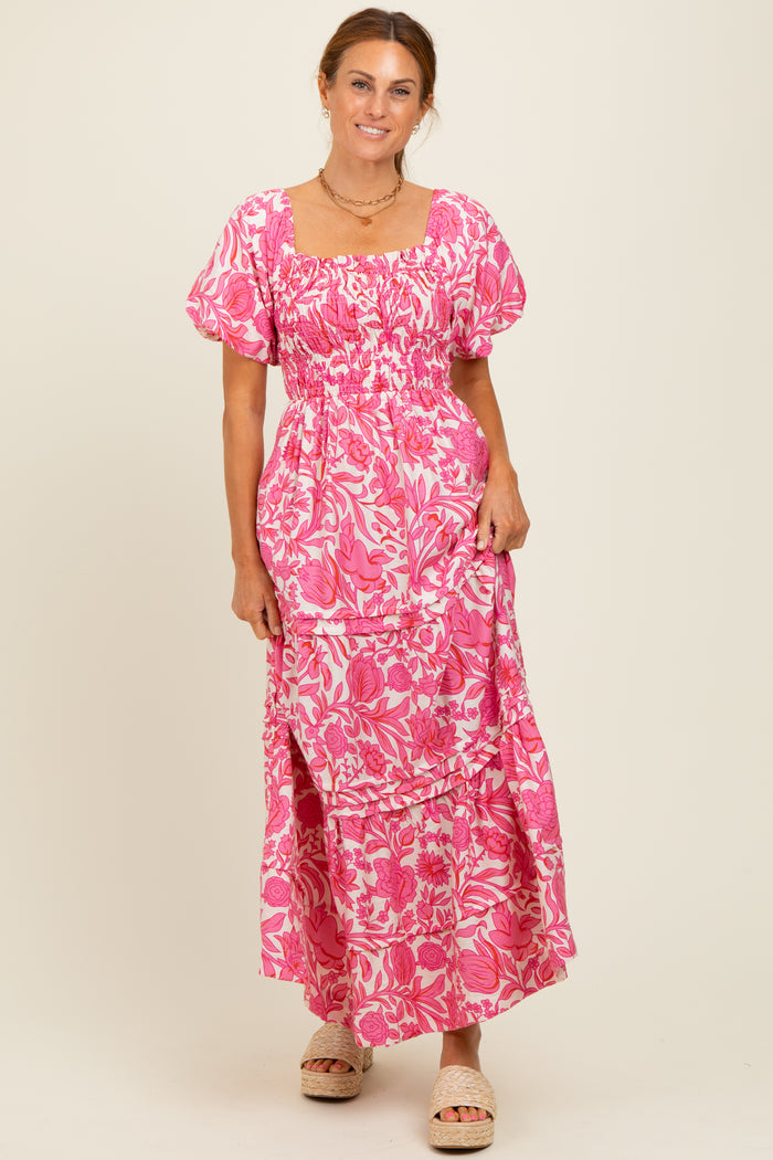 woman wearing a pink floral maxi dress with puff sleeves and a square neckline, standing and smiling