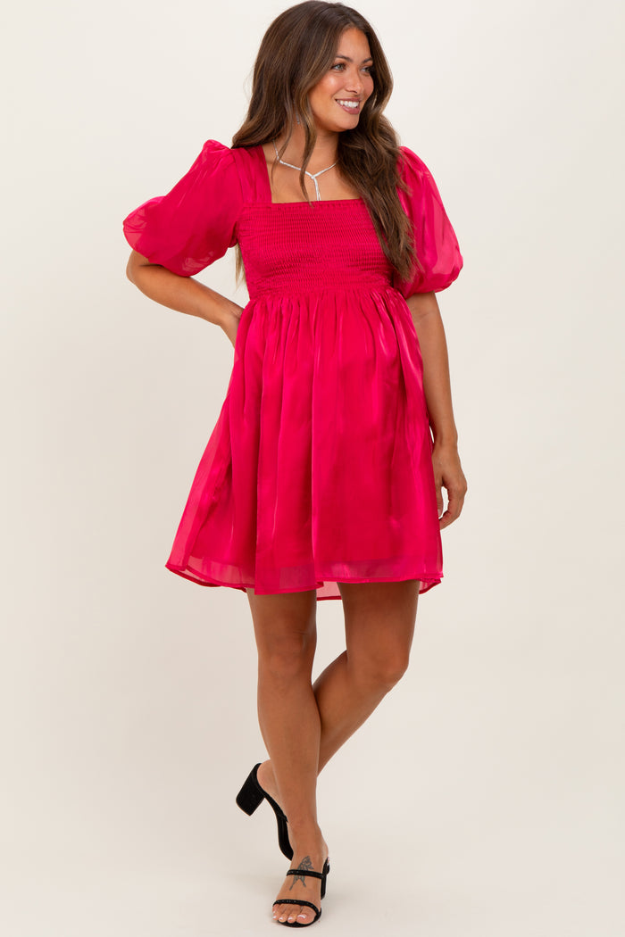 woman wearing a bright pink maternity dress with puff sleeves and a smocked bodice, standing and smiling