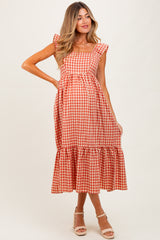 woman wearing a red and white gingham maternity dress with ruffled sleeves and a tiered skirt, showing her baby bump