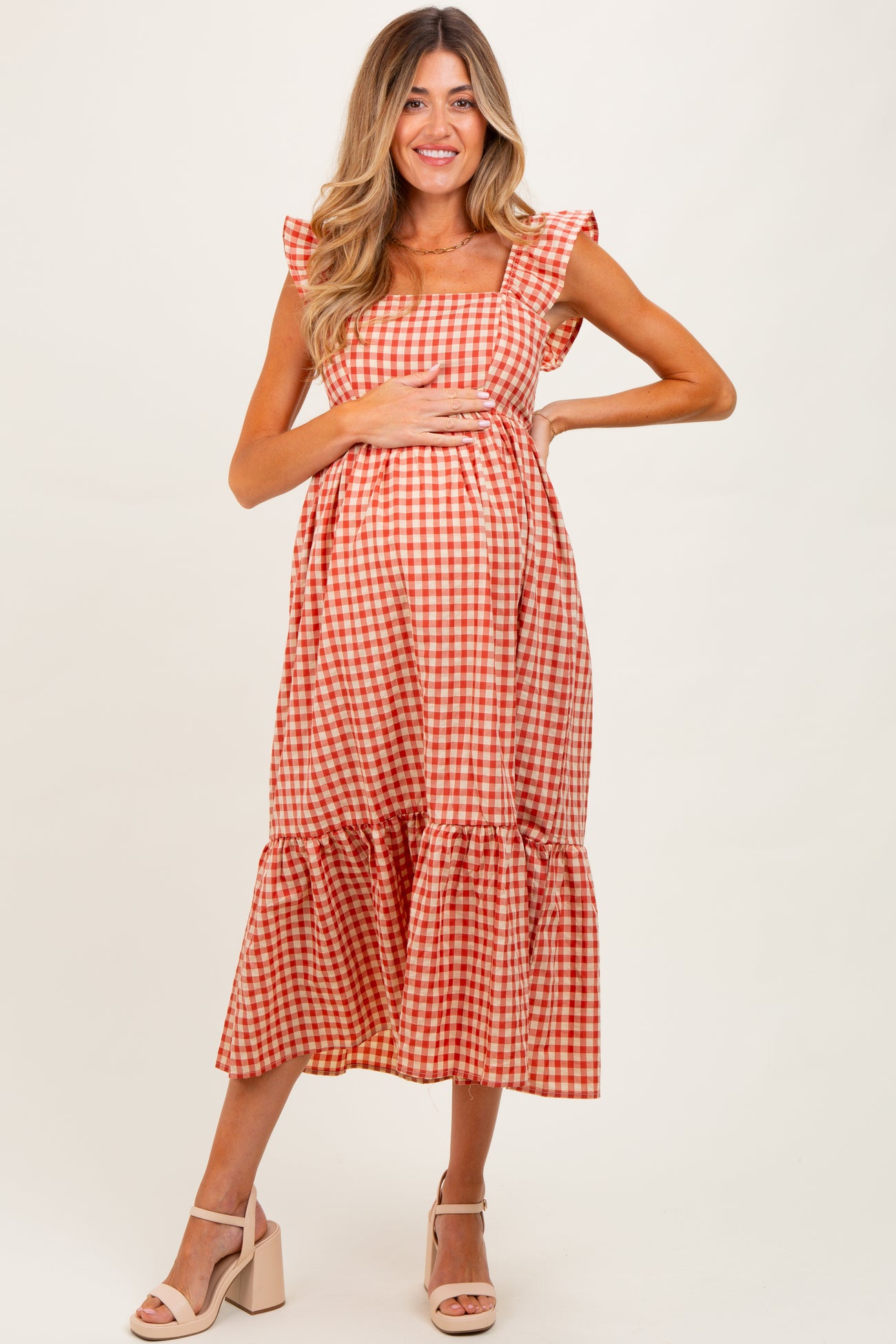 woman wearing a red and white gingham maternity dress with ruffle sleeves and a tiered skirt, showing her baby bump