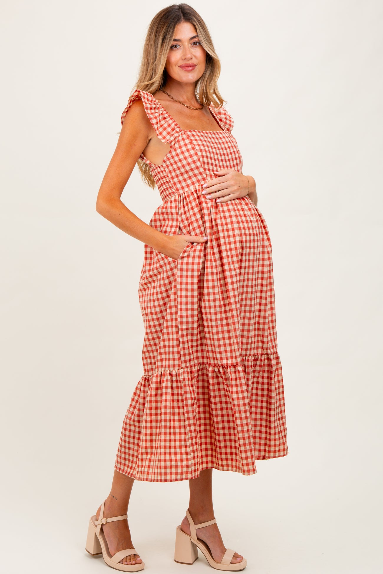 woman wearing a red and white gingham maternity dress with ruffles and a tiered skirt, holding her baby bump
