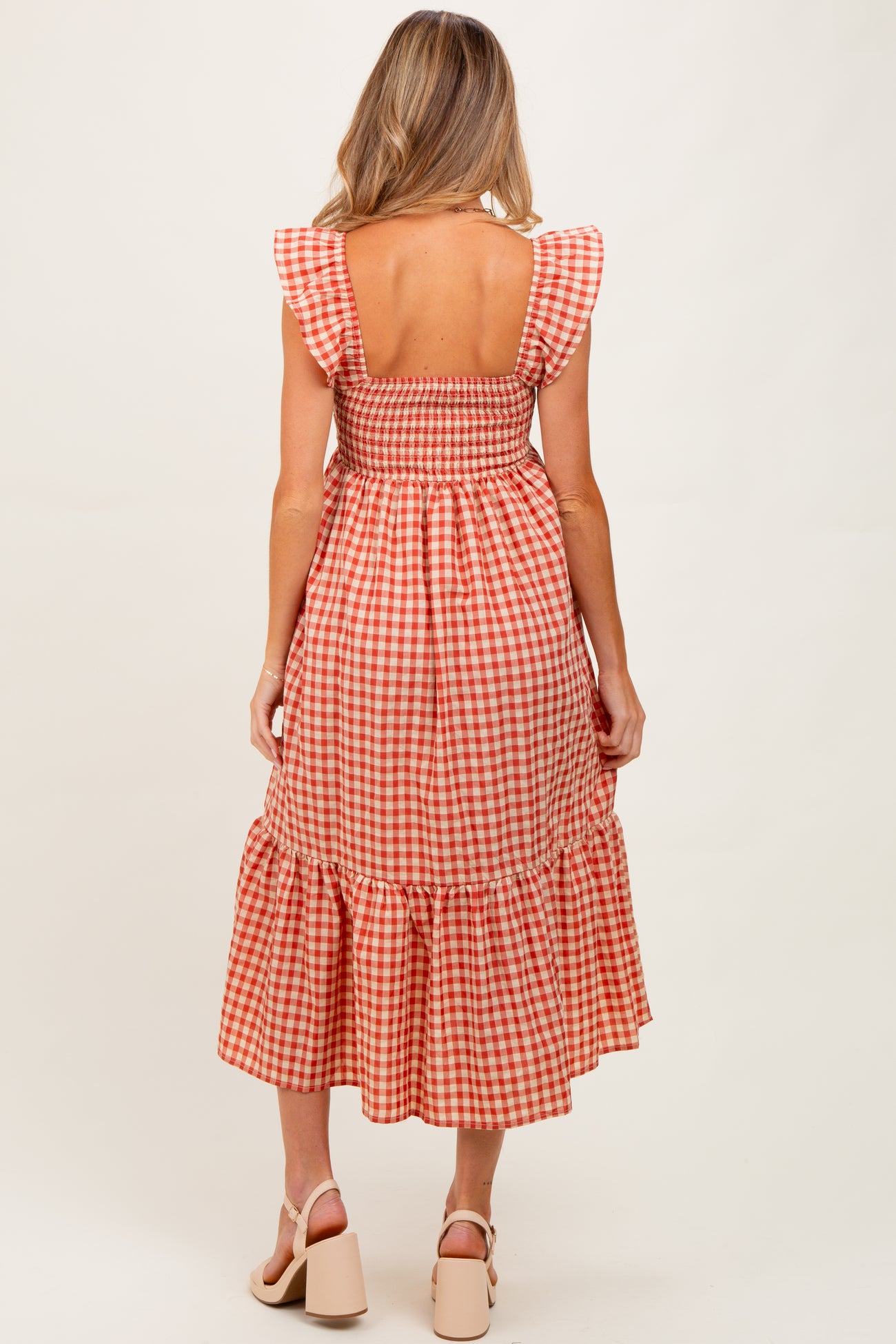 woman wearing a red and white gingham maternity dress with ruffled sleeves and a smocked bodice, showing a baby bump
