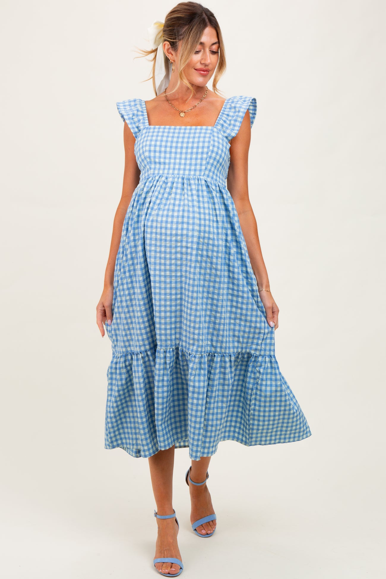woman wearing a blue gingham maternity dress with ruffled sleeves and a tiered skirt, showing her baby bump
