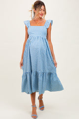 woman wearing a blue gingham maternity dress with ruffled sleeves and a tiered skirt, showing her baby bump
