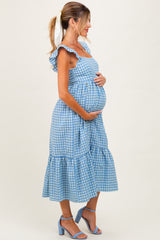 woman wearing a blue gingham maternity dress with ruffle straps and a flowy skirt, holding her baby bump