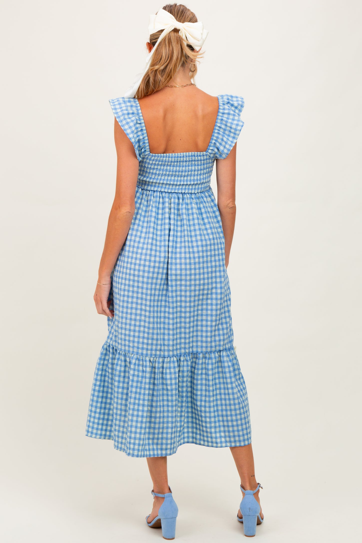 woman wearing a blue gingham midi maternity dress with ruffle sleeves, showing a baby bump from the back