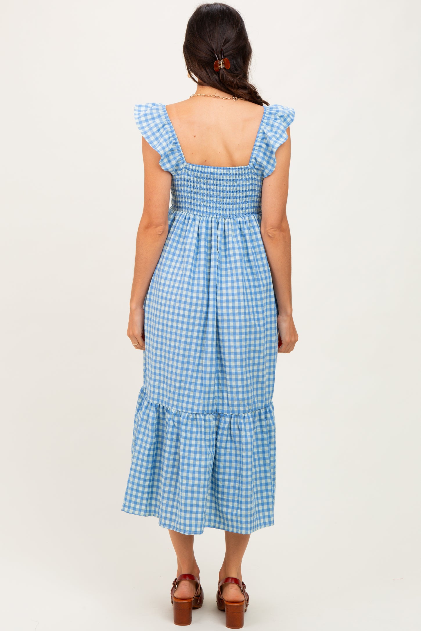 woman wearing a blue gingham smocked midi dress with ruffle straps and a tiered skirt, viewed from the back