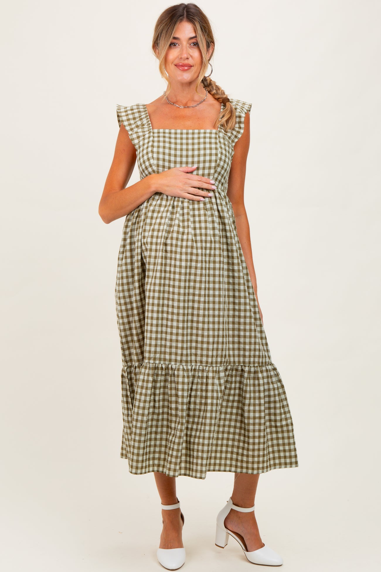 woman wearing a green and white gingham maternity dress with ruffle sleeves and a gathered skirt, holding her baby bump