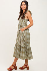 woman wearing a green and white gingham midi dress with ruffle straps and pockets, paired with brown block-heeled sandals