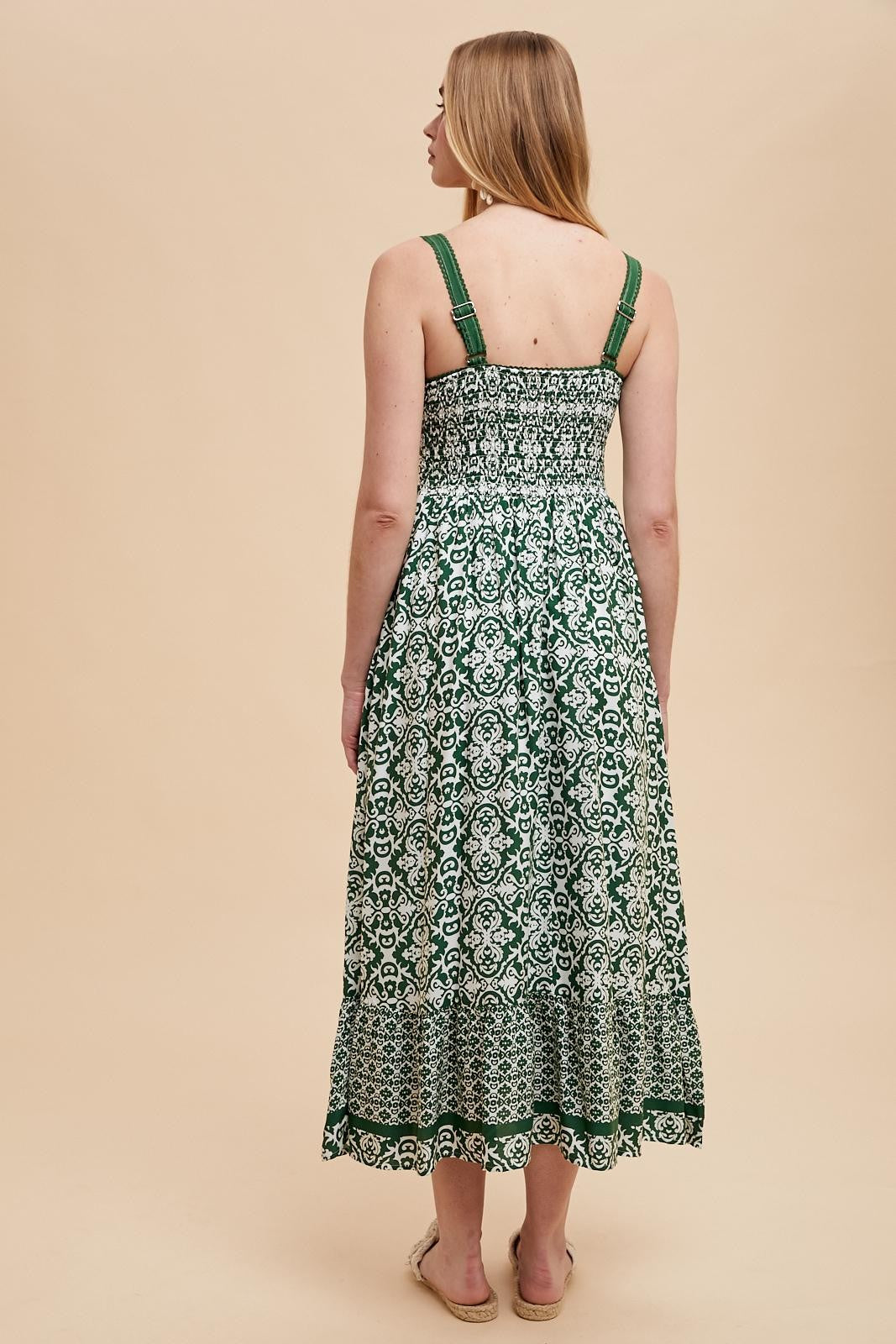 woman wearing a green floral maxi dress with smocked back and adjustable straps, standing against a neutral background