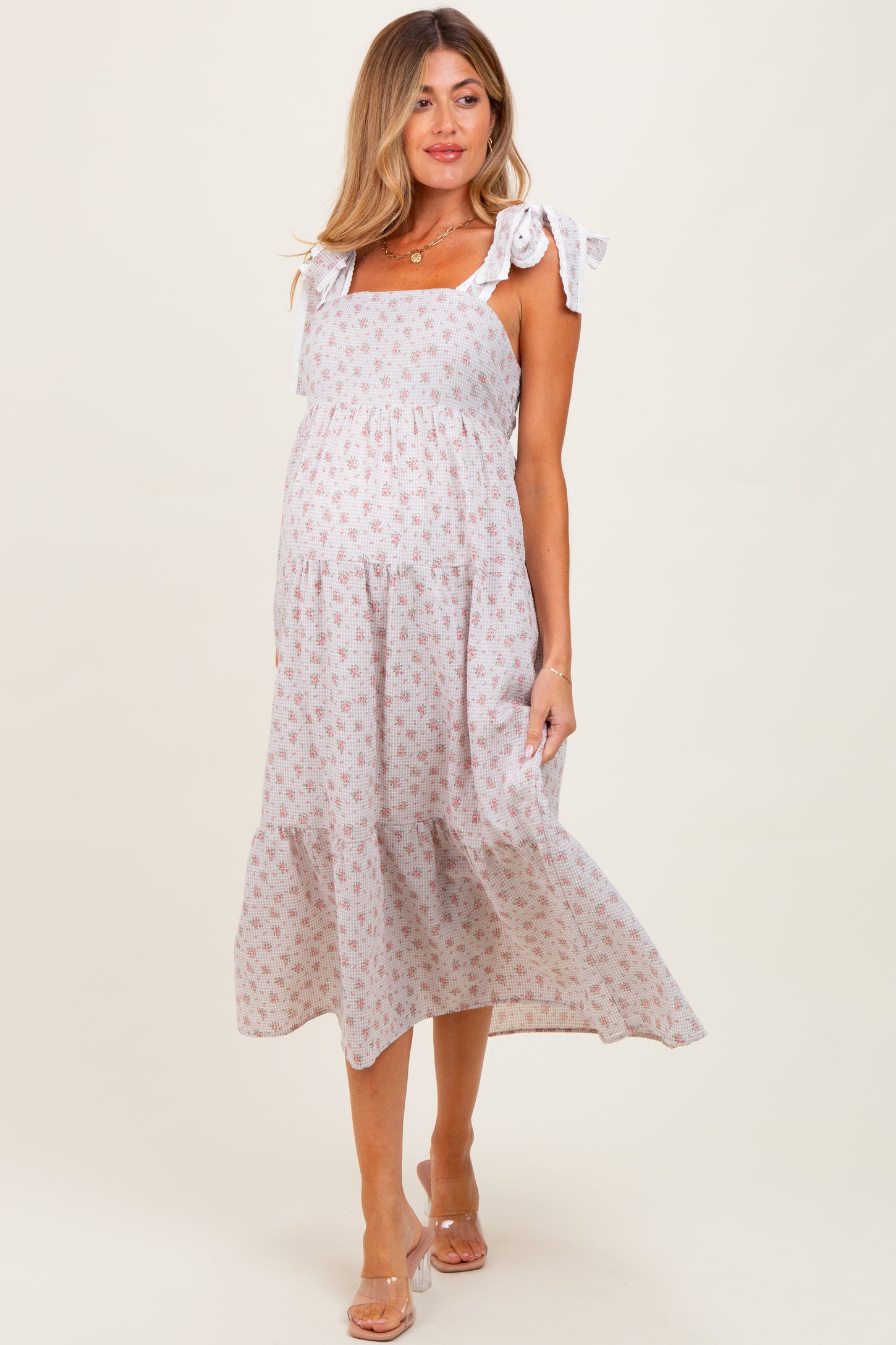 woman wearing a light floral maternity dress with adjustable tie straps and a flowing skirt, showing her baby bump