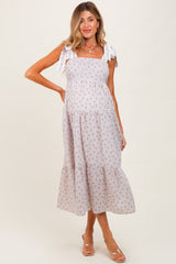 woman wearing a light pink floral print maternity dress with adjustable tie straps and a tiered skirt, showing her baby bump
