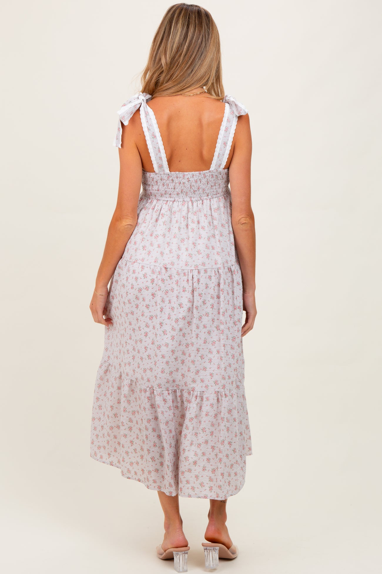 woman wearing a flowy white floral maternity dress with tie straps and a smocked bodice, showing her back