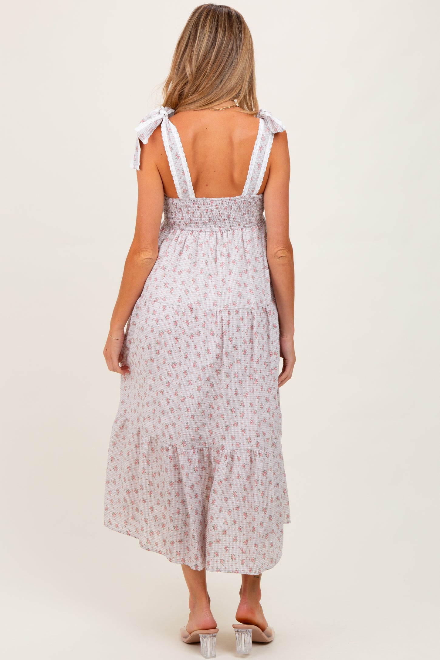 woman wearing a flowy white floral maternity dress with tie straps and a smocked bodice, showing her back