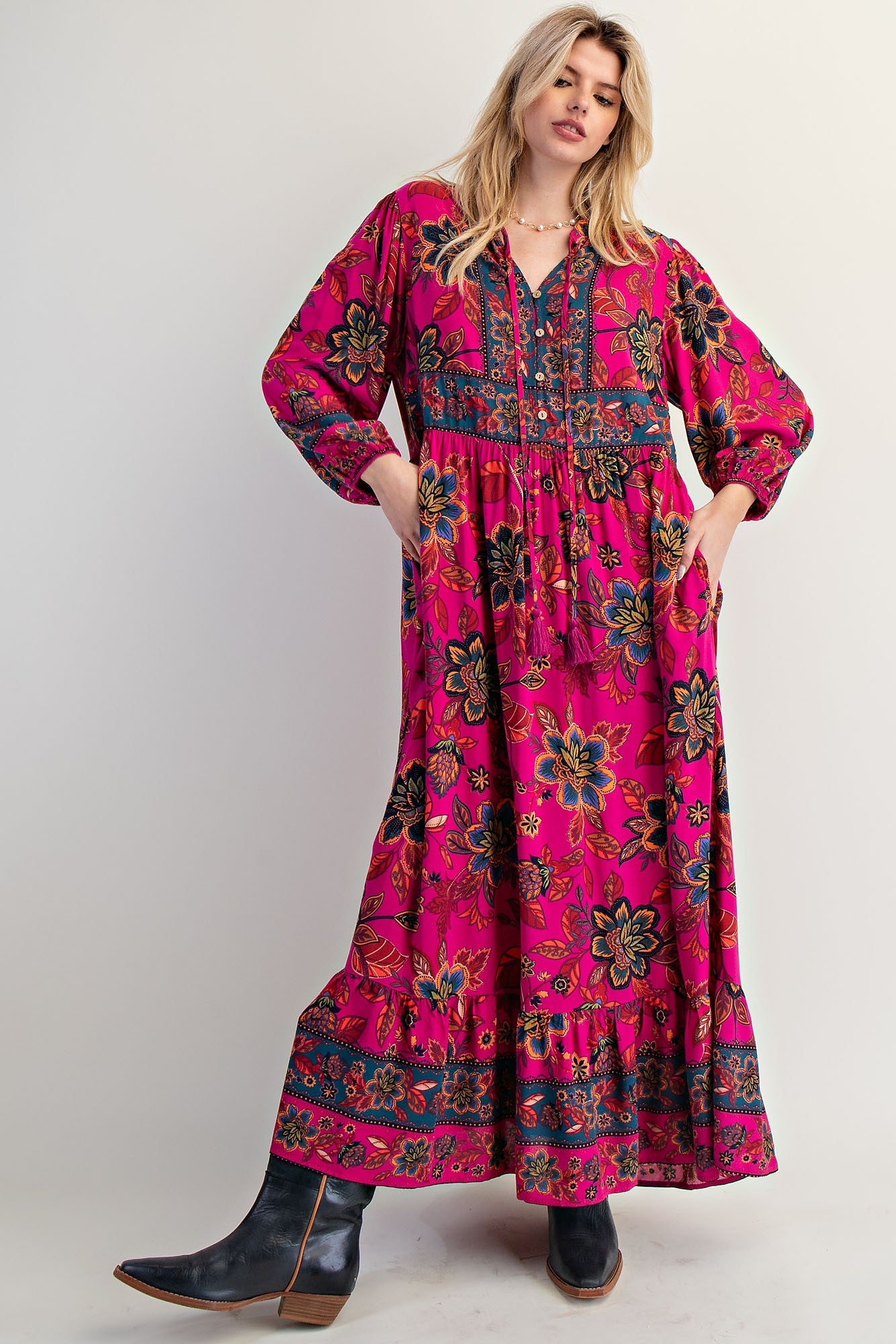 woman wearing a bright pink floral maxi dress with pockets and long sleeves, styled with ankle boots