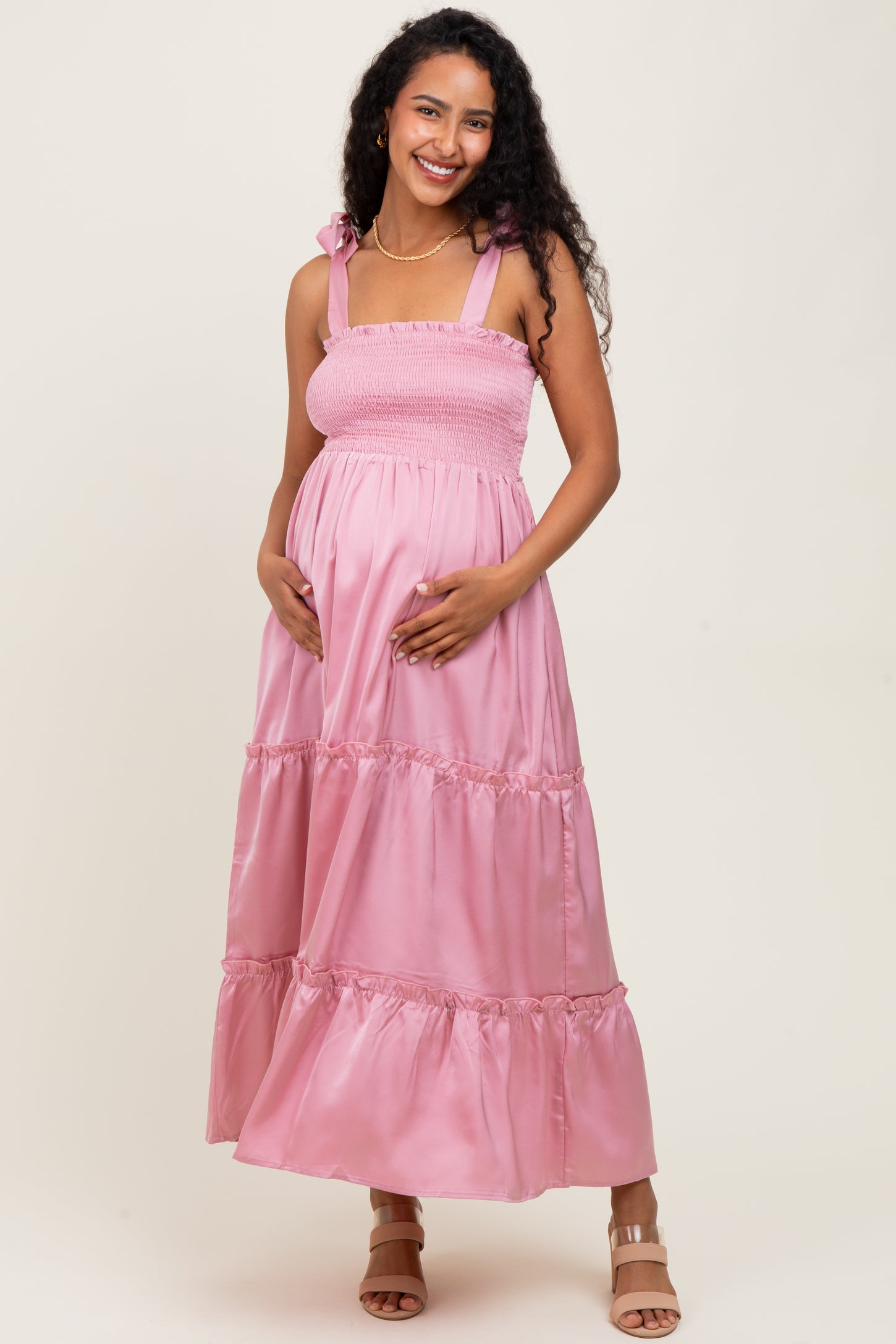 woman wearing a light pink maternity maxi dress with smocked bodice and tiered skirt, holding her baby bump