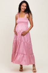 woman wearing a light pink maternity maxi dress with smocked bodice and tiered skirt, holding her baby bump