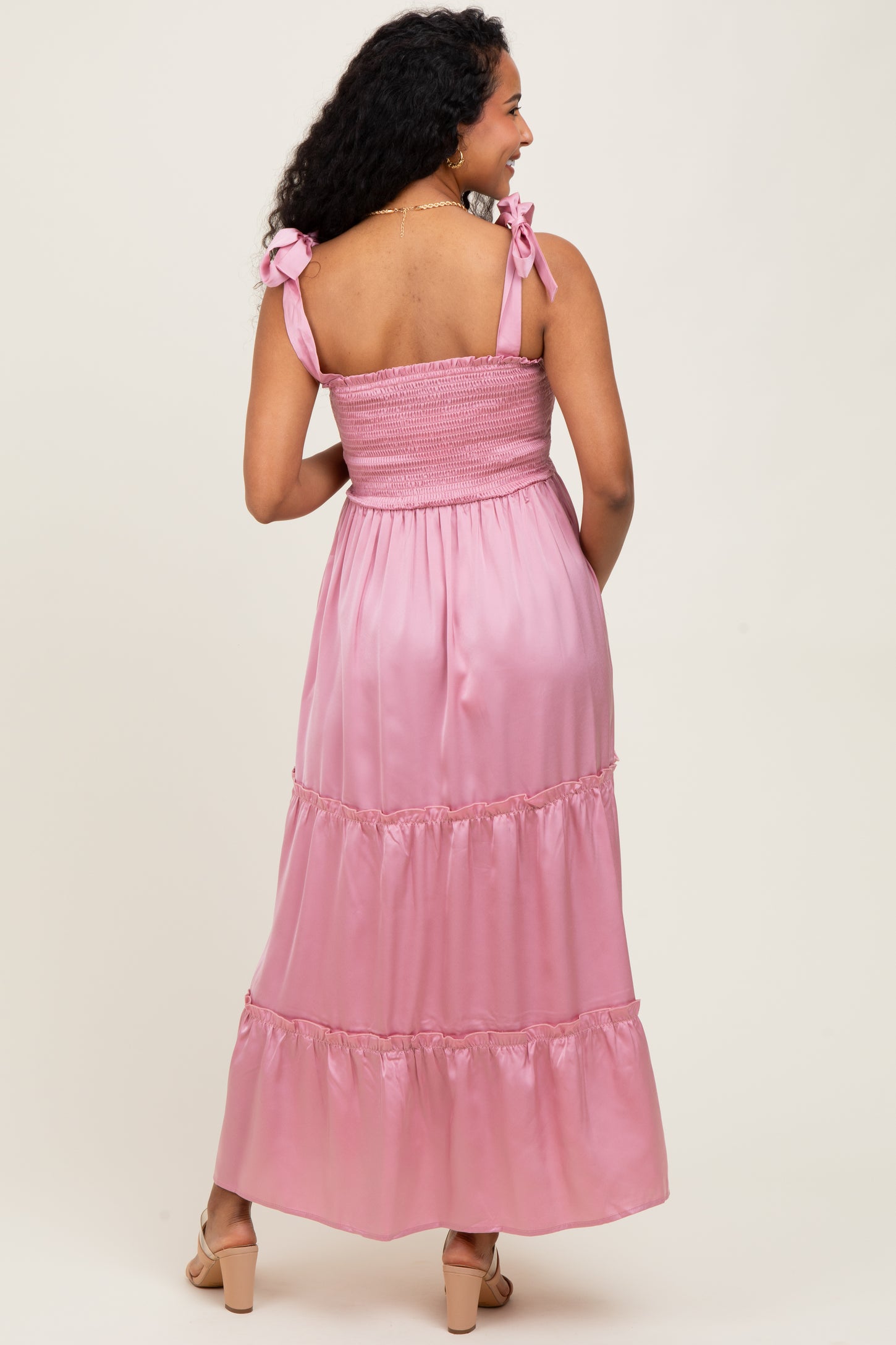 woman wearing a pink maternity maxi dress with smocked bodice and bow details on shoulder straps, showing her baby bump