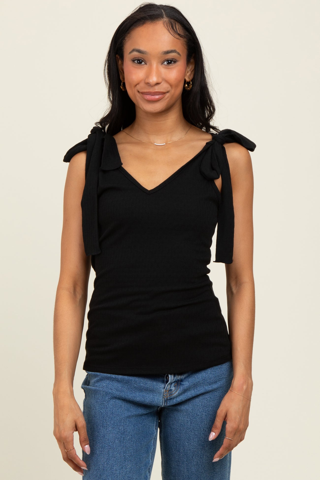 woman wearing a black ribbed tank top with bow tie shoulder accents and blue jeans