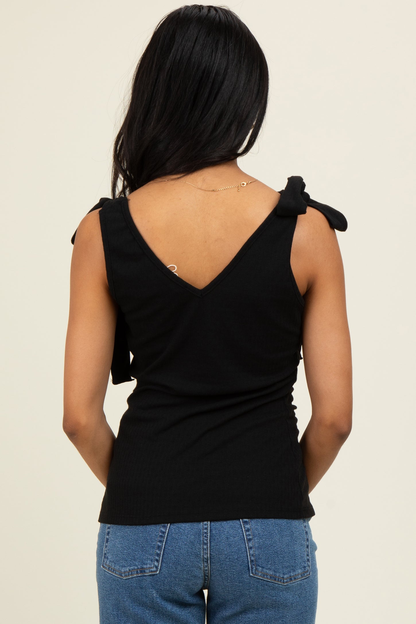 woman wearing a black sleeveless top with tie shoulder details and a v-back, paired with blue jeans