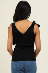 woman wearing a black sleeveless top with tie shoulder details and a v-back, paired with blue jeans