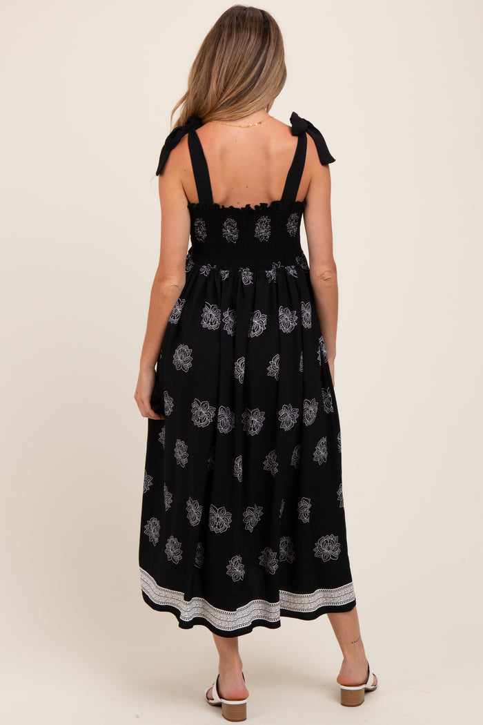 woman wearing a black maternity dress with floral print and tie straps, showing the back and smocked bodice detail