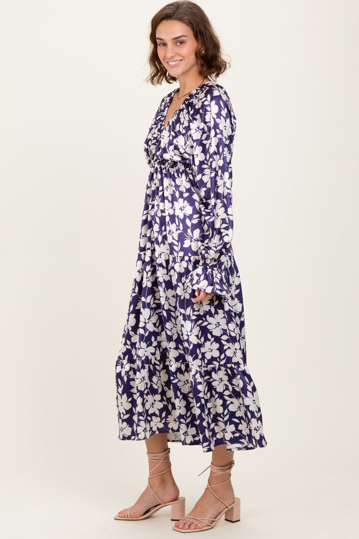 woman wearing a purple floral maxi dress with long sleeves and a v-neckline, standing elegantly against a neutral background