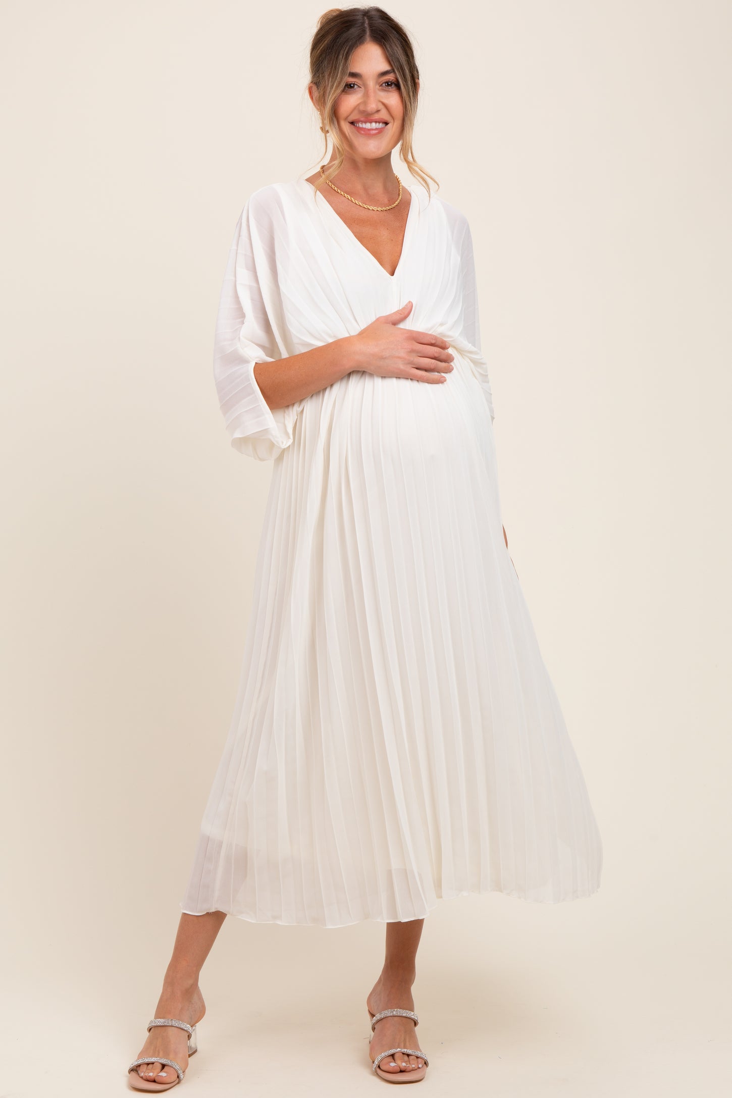 woman wearing a white pleated maternity dress and holding her baby bump