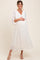 woman wearing a white pleated maternity dress and holding her baby bump