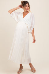woman wearing a white pleated maternity dress with a v-neckline and flowy sleeves, showcasing her baby bump