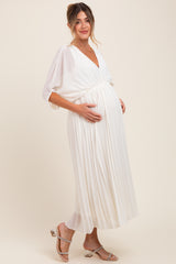 woman wearing a white pleated maternity maxi dress and holding her baby bump