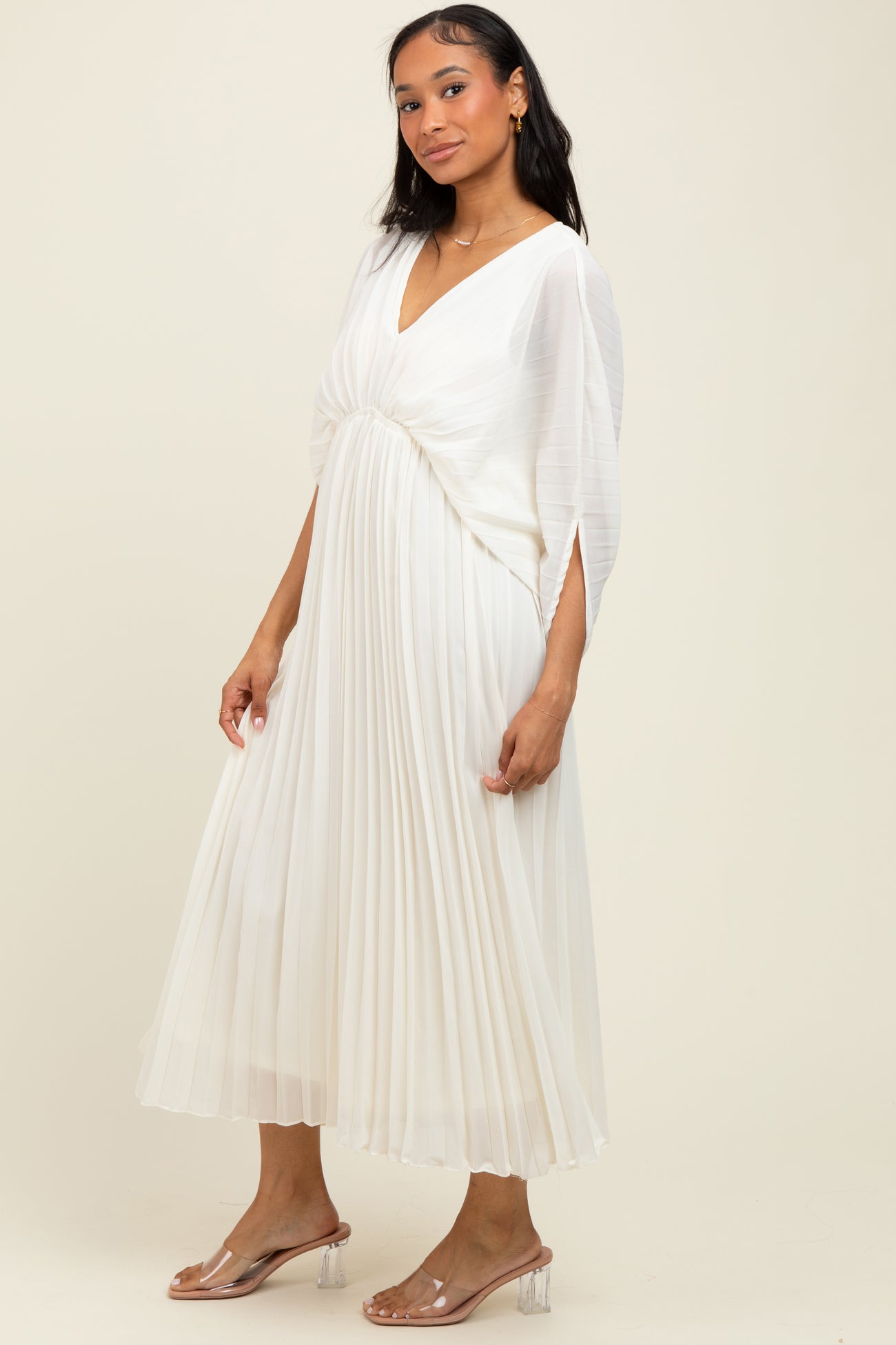 woman wearing a white pleated maxi dress with a v-neck and short sleeves, styled with clear heeled sandals