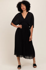 woman wearing a black pleated maxi dress with a deep v-neck and flutter sleeves