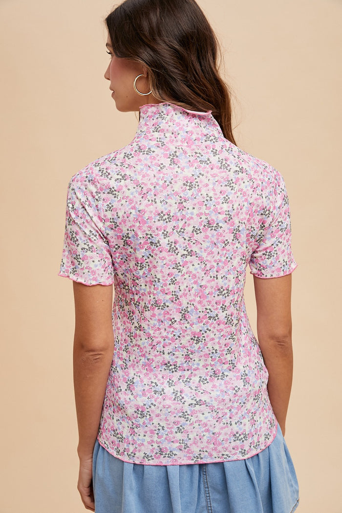 woman wearing a pink floral short sleeve top with a high neckline and a relaxed fit, viewed from the back