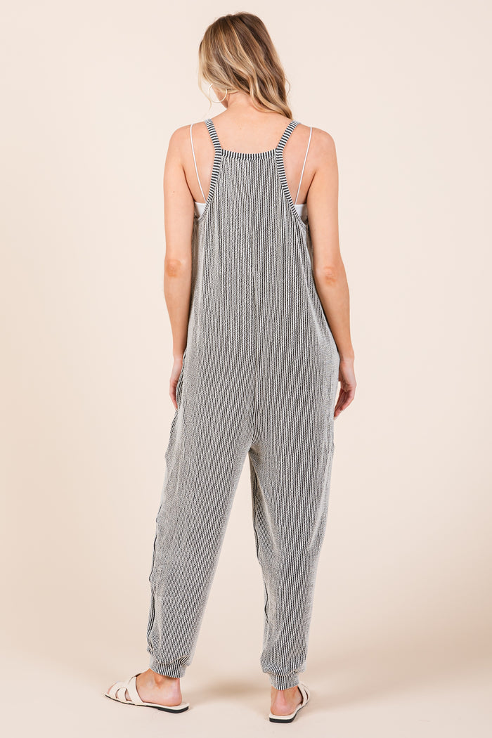woman wearing a gray and white striped cotton jumpsuit with adjustable straps and tapered legs, shown from the back