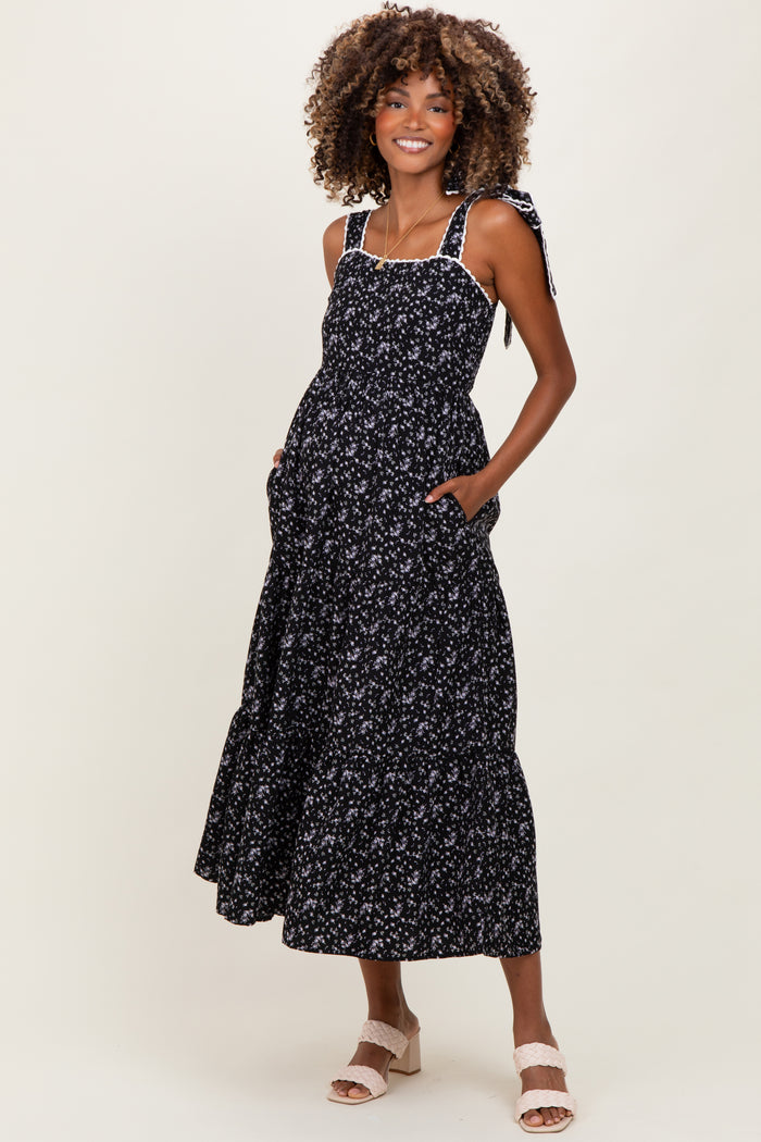 woman wearing a black floral maternity maxi dress with tie shoulder straps and pockets, showing baby bump