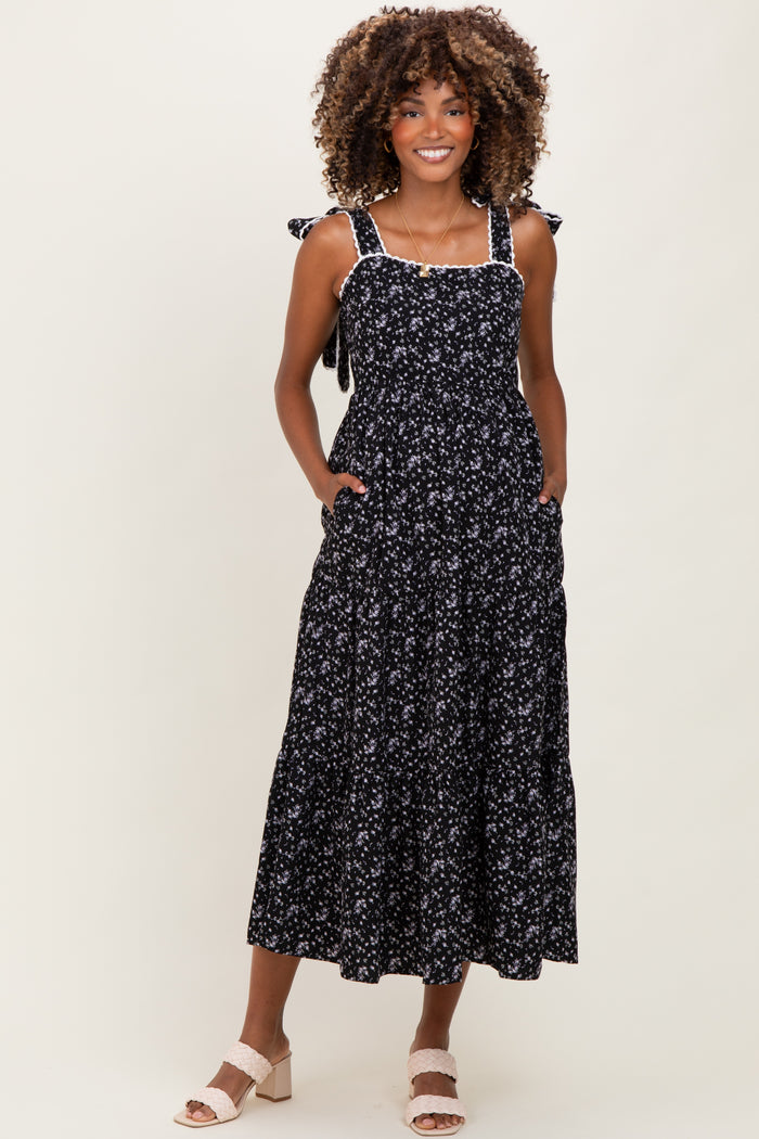 woman wearing a black floral print maternity dress with tie straps and pockets, showcasing a baby bump