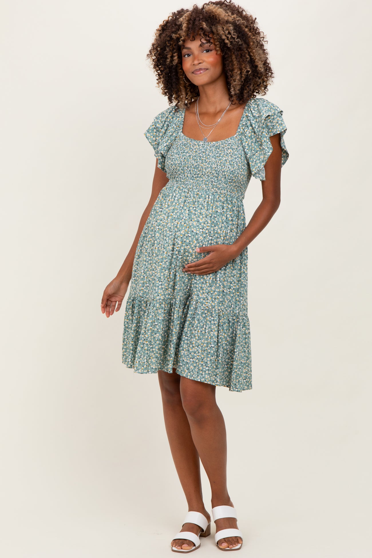 woman wearing a green floral maternity dress with ruffled sleeves and a tiered hem, holding her baby bump