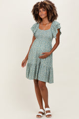 woman wearing a green floral maternity dress with ruffled sleeves and a tiered hem, holding her baby bump